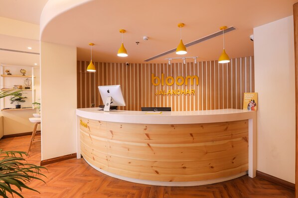 Un comptoir d’accueil avec un revêtement en bois, un écran d’ordinateur et une enseigne sur laquelle on peut lire « Bloom Jalandhar ».