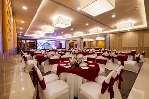 Salão de banquetes com mesas redondas, cadeiras brancas e toalhas de mesa vermelhas.