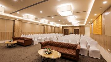 Un salón de conferencias con filas de sillas blancas, un sofá marrón y dos mesitas con centros de mesa florales.