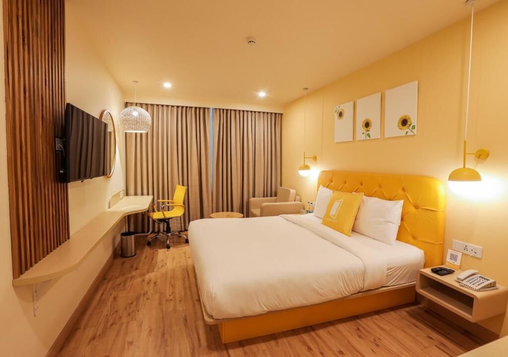 A hotel room with a bed, bedside table, lamp, and a desk with a chair.