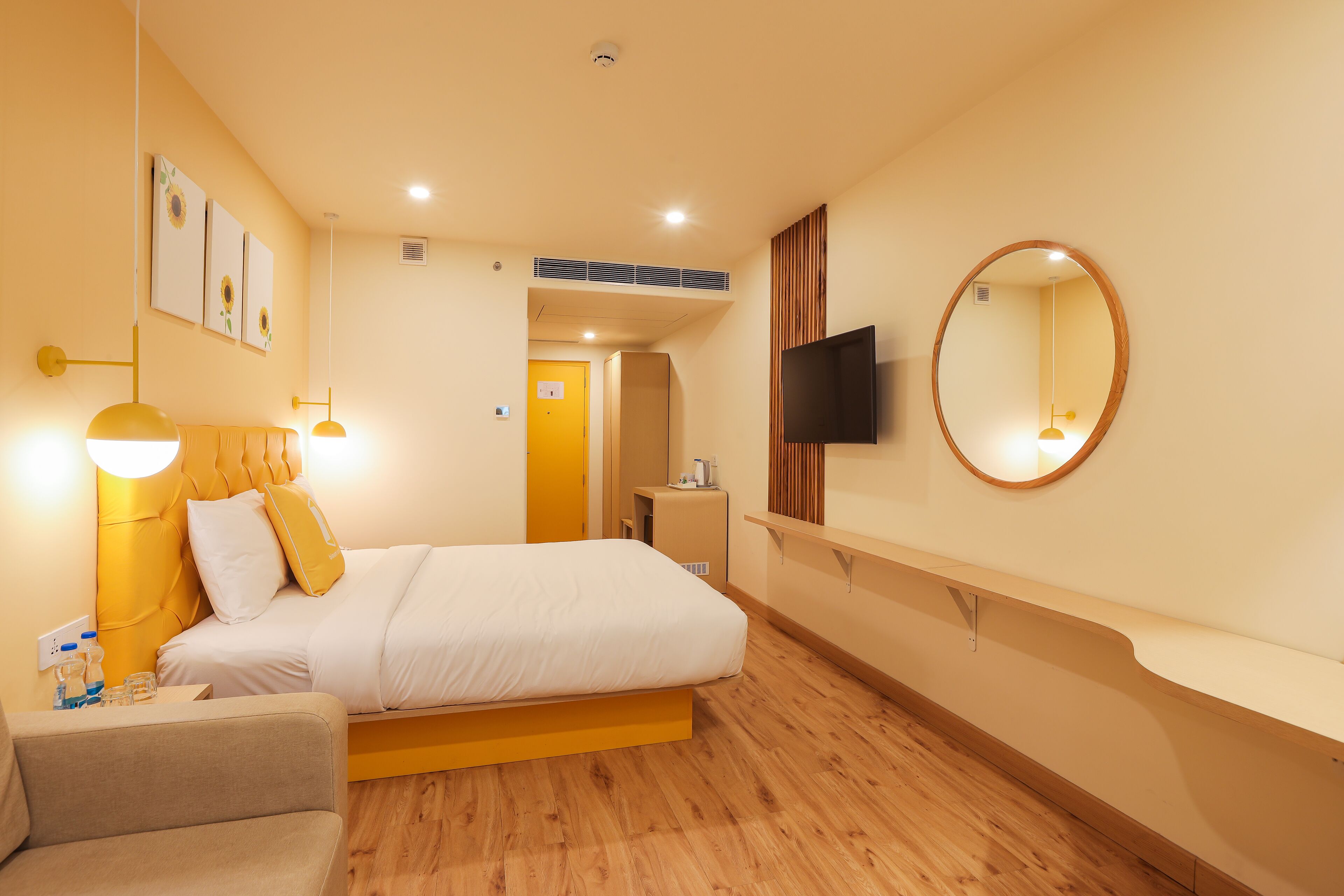 A hotel room with a bed, bedside table, lamp, and a TV mounted on the wall.