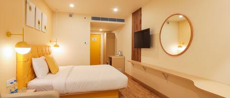 A hotel room with a bed, bedside table, lamp, and a TV mounted on the wall.