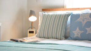 Een net opgemaakt bed met streepjesbeddengoed, een bedlampje en een tijdschrift op het nachtkastje.