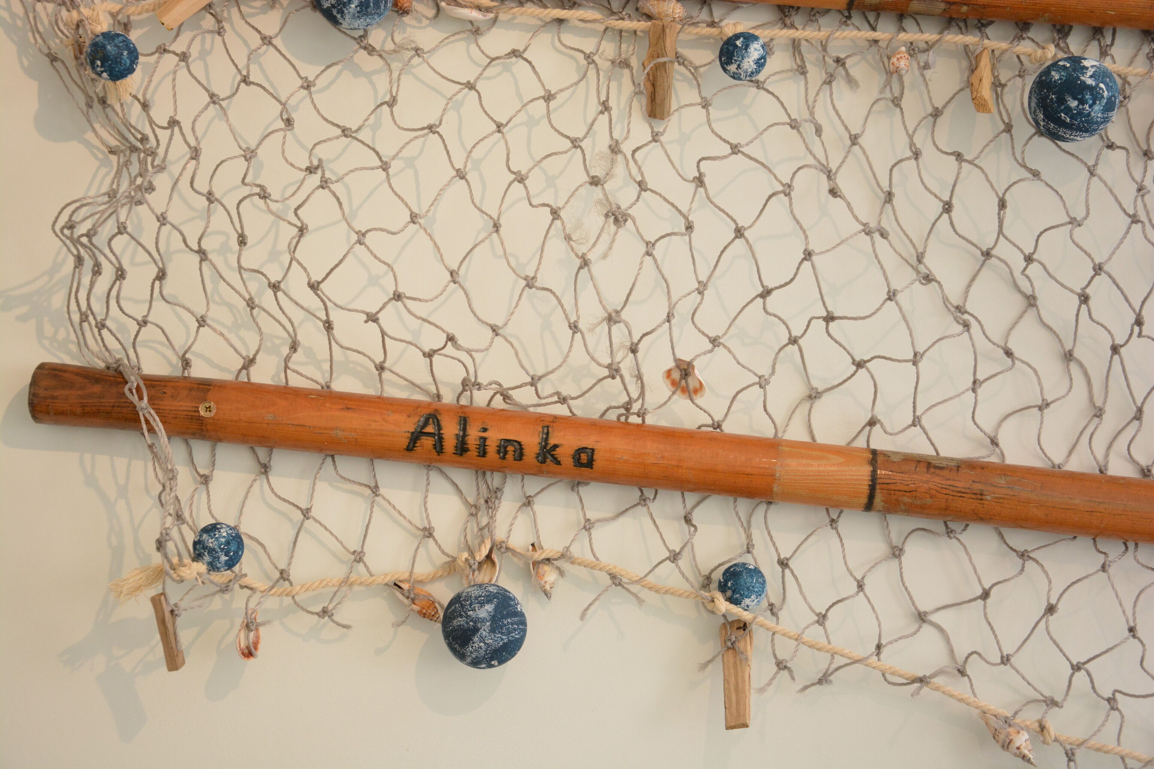 A wooden bat labeled "Alinka" hanging on a net with blue and white spherical objects.