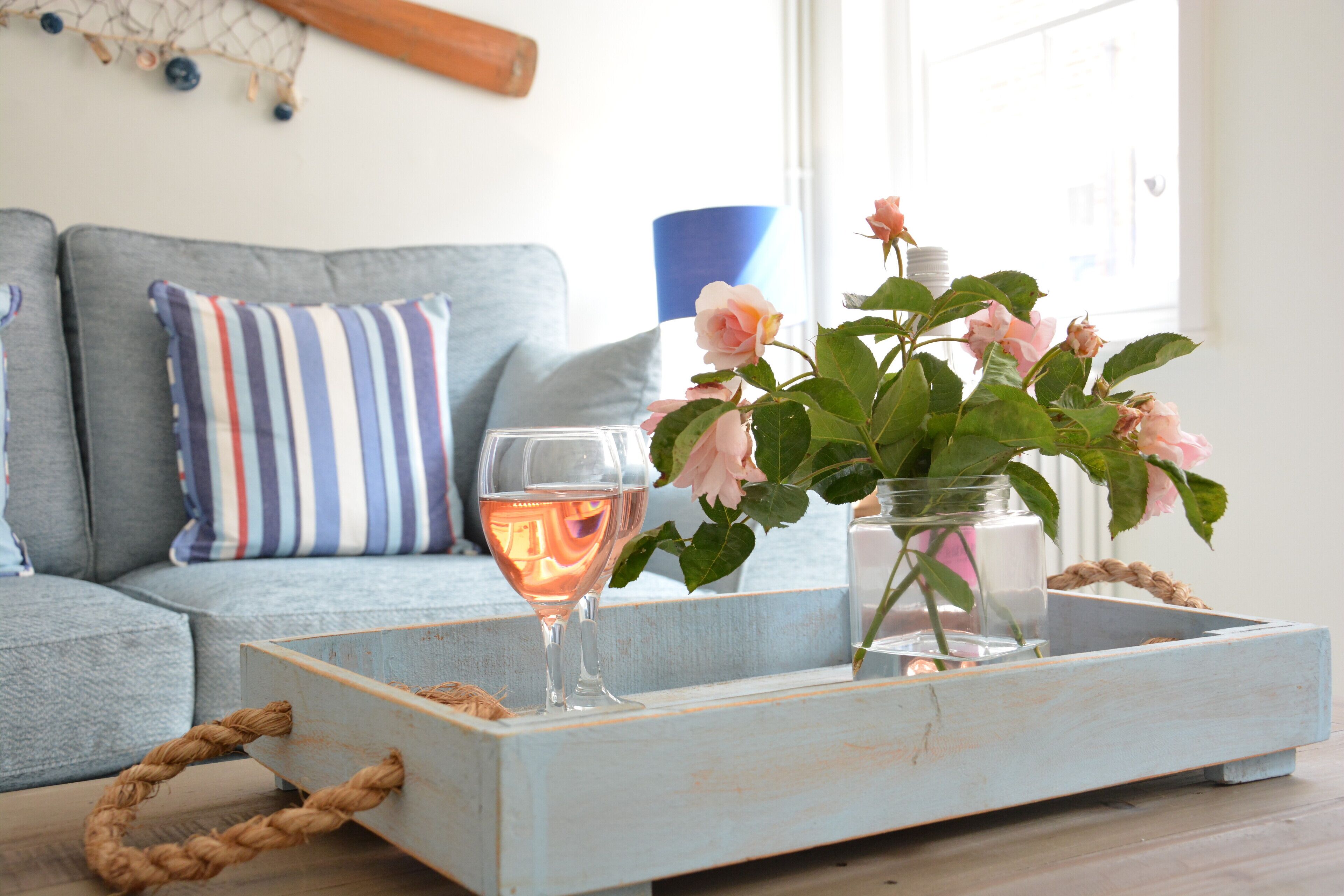 Un vassoio di legno con un bicchiere di vino rosa e un vaso di rose rosa su un tavolo di legno.