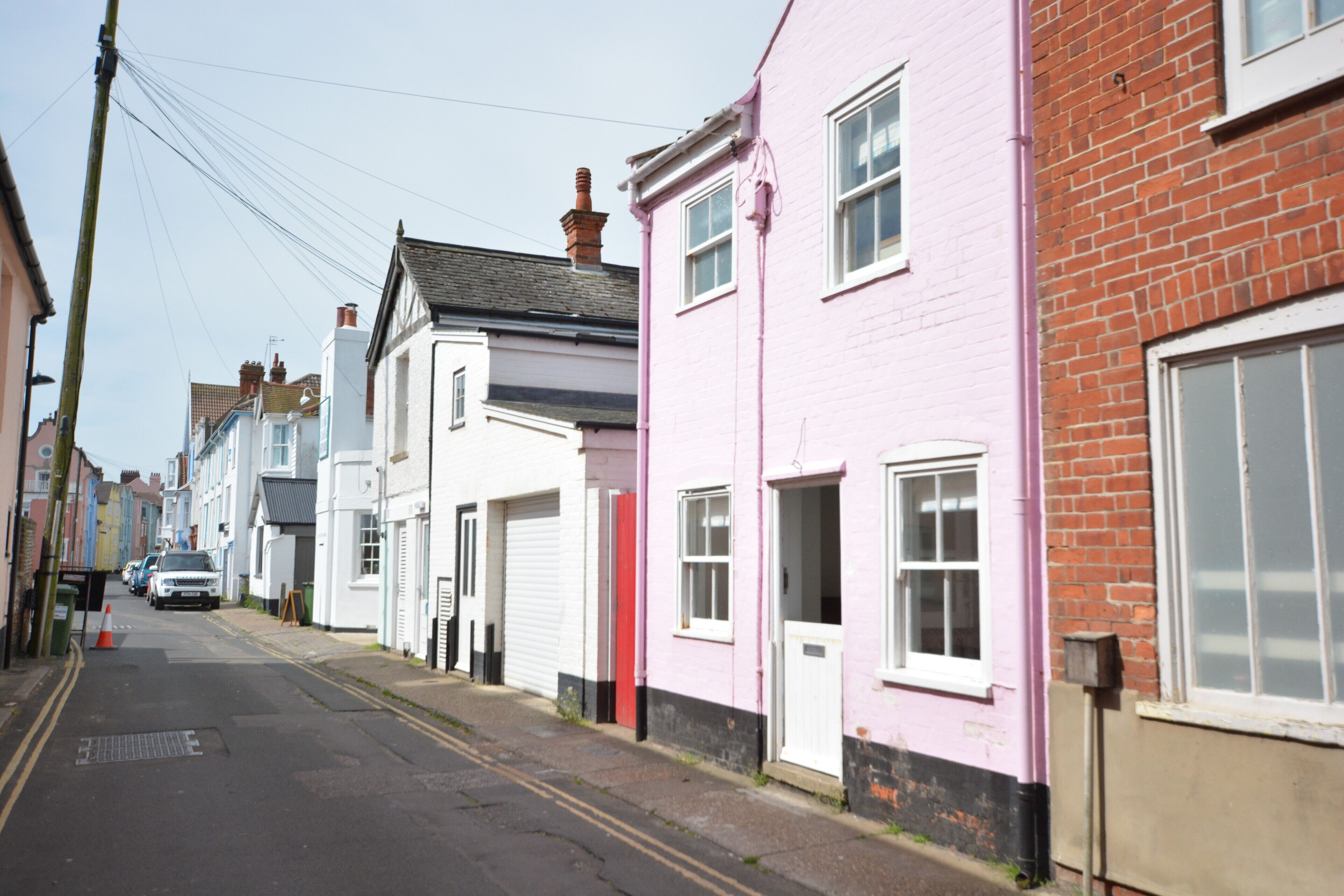 Een smalle straat met aan weerszijden traditionele huizen, waarvan sommige roze en witte gevels hebben, en een heldere lucht erboven.