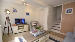 Een woonkamer met een televisie, een statief, een stoel, een salontafel met decoratieve objecten en een trap.