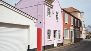 Een rij herenhuisen met verschillende pastelkleuren, een witte garage deur en een heldere straat.