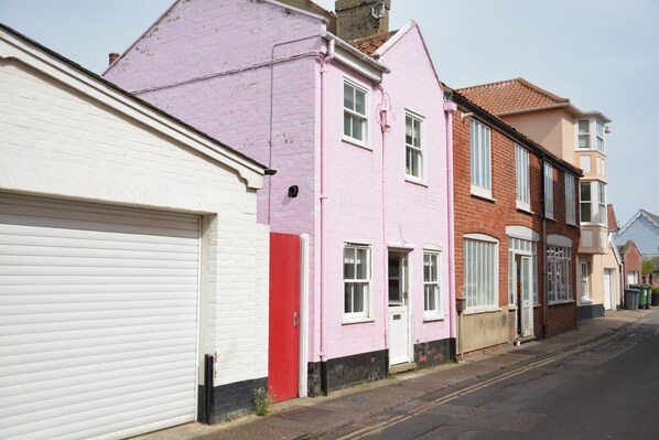 A row of terraced houses with distinct pastel colors, a white garage door, and a clear street.