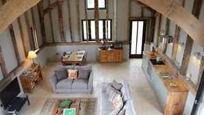 A spacious living area with a sofa, coffee table, and a dining table. A kitchen area with a sink and stove is visible. - Manor House Barn, Peasenhall (Saxmundham)