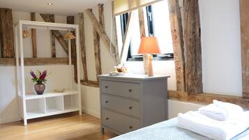 Un dormitorio con cama, cómoda, tocador, ventana y estructura de vigas de madera.
