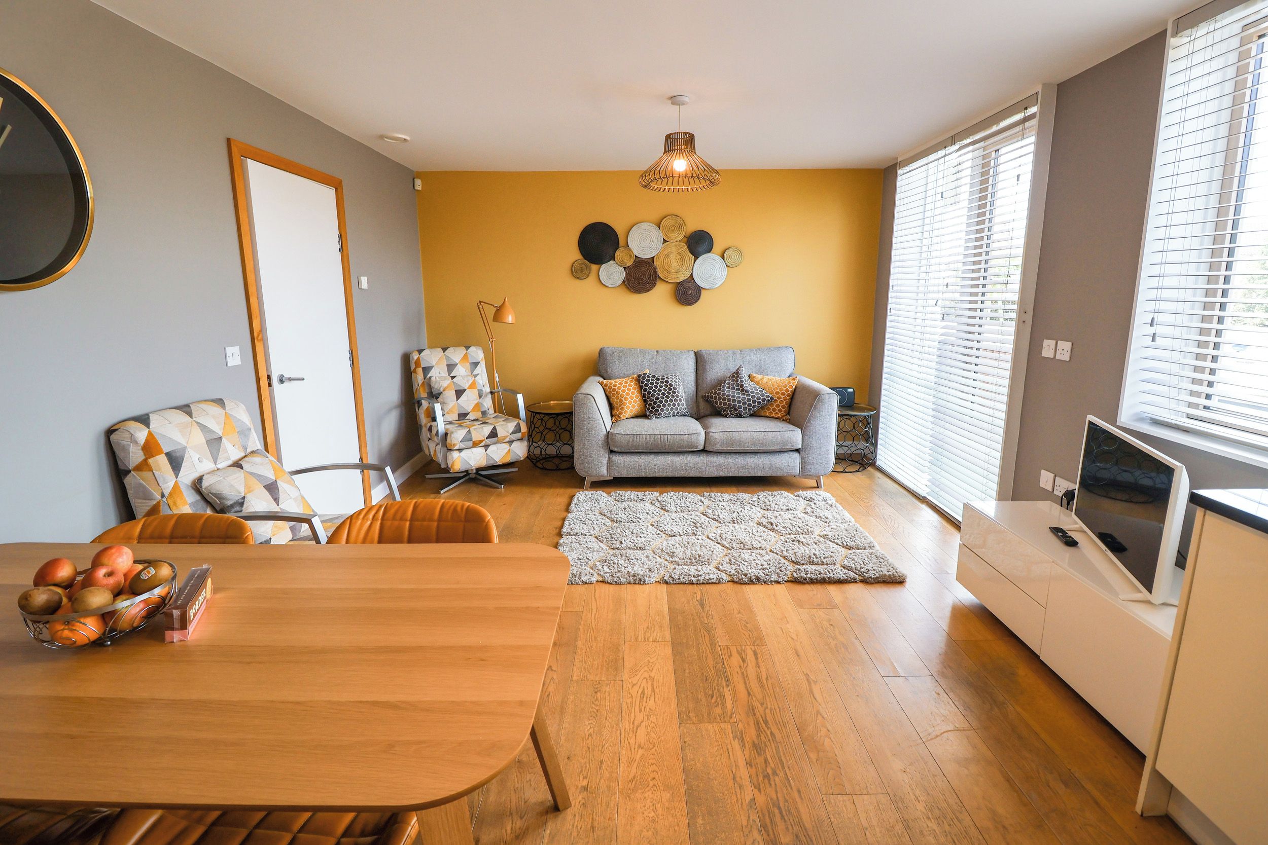A modern living room with a sofa, a dining table with fruit, and a TV.
