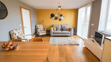 A modern living room with a sofa, a dining table with fruit, and a TV.
