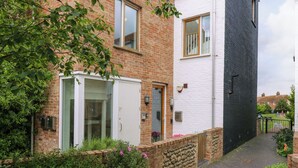 Un immeuble résidentiel à la façade en briques, avec une porte blanche et un petit jardin agrémenté de fleurs roses.