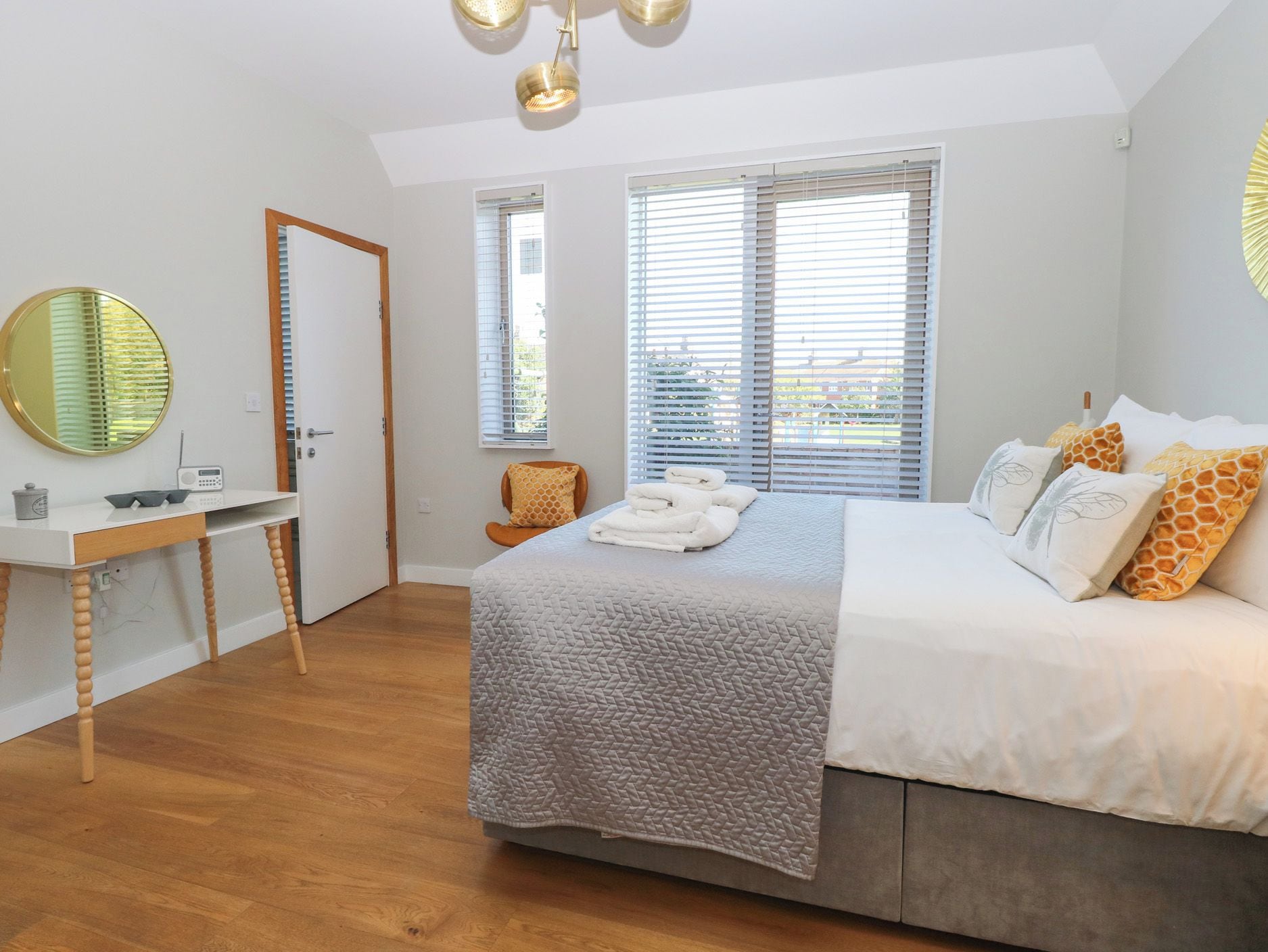 Un dormitorio con cama, escritorio, silla y un amplio ventanal con persianas.