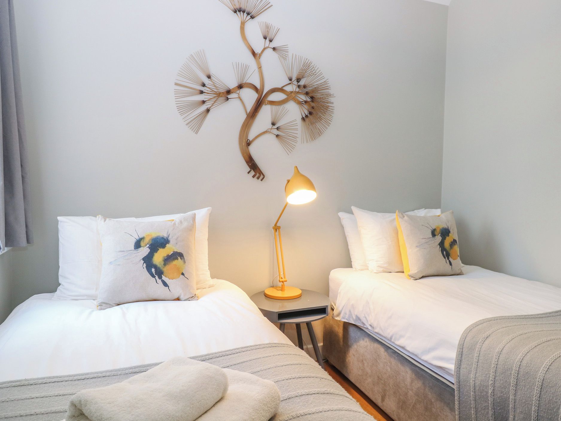 A hotel room with two beds, a bedside table with a lamp, and a wall decoration.