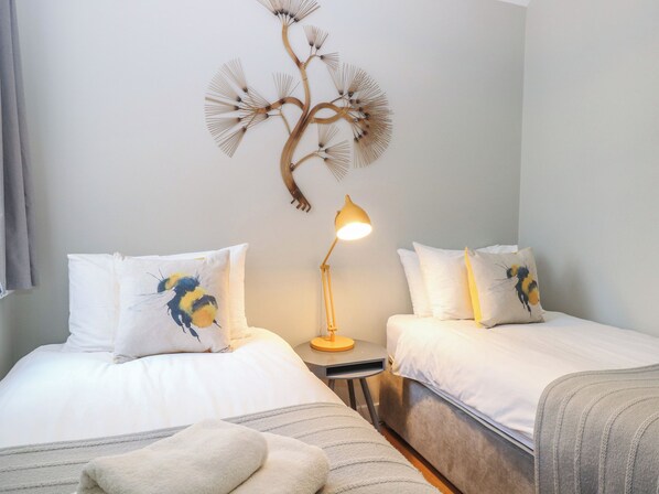 A hotel room with two beds, a bedside table with a lamp, and a wall decoration. - The Hive, Southwold (Reydon)