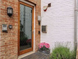 Una casa de ladrillo con puerta de madera, ventana de vidrio y un pequeño jardín con flores rosadas.
