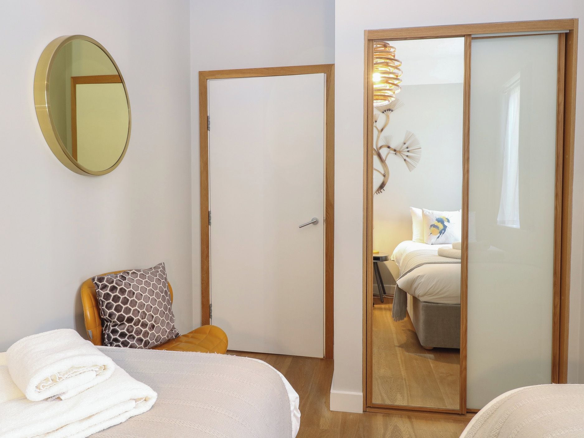 Un dormitorio con una cama, un espejo redondo, una puerta y una vista a otra habitación a través de un espejo.