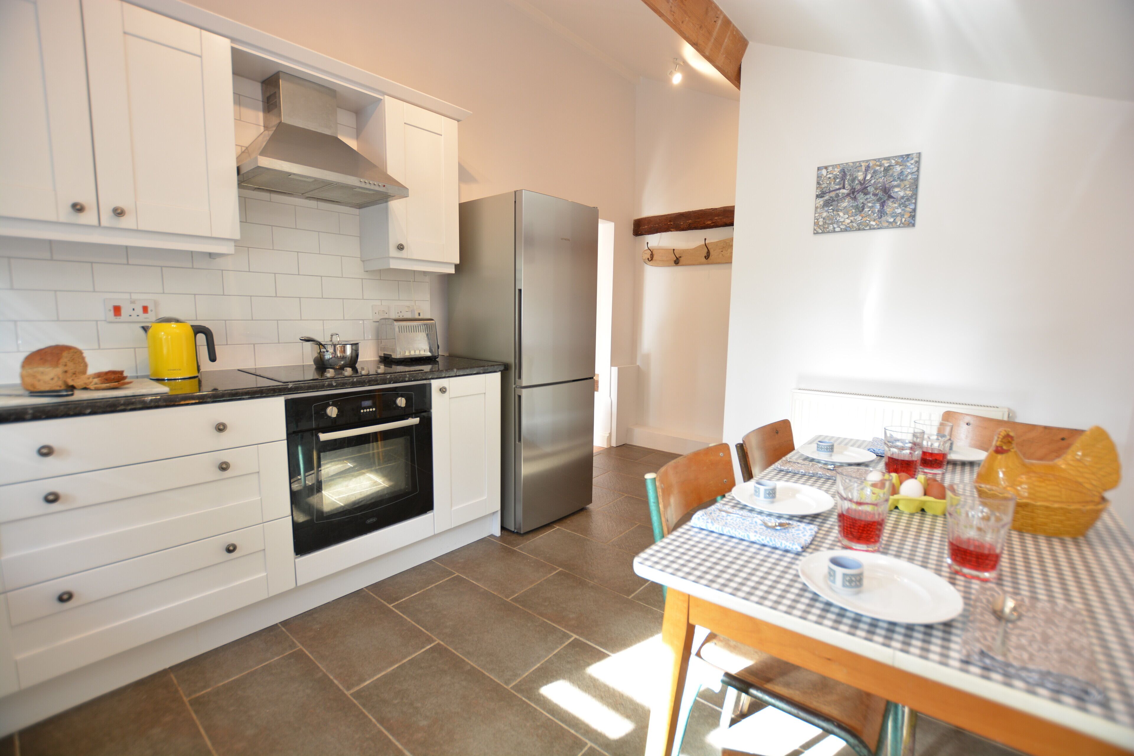 Una cocina moderna con armarios blancos, un refrigerador de acero inoxidable y una mesa de comedor preparada para cuatro.