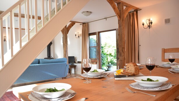 A dining area with a wooden table set for a meal, a blue sofa in the background, and a staircase leading to an upper level. - Wheelwright's Barn (Halesworth)