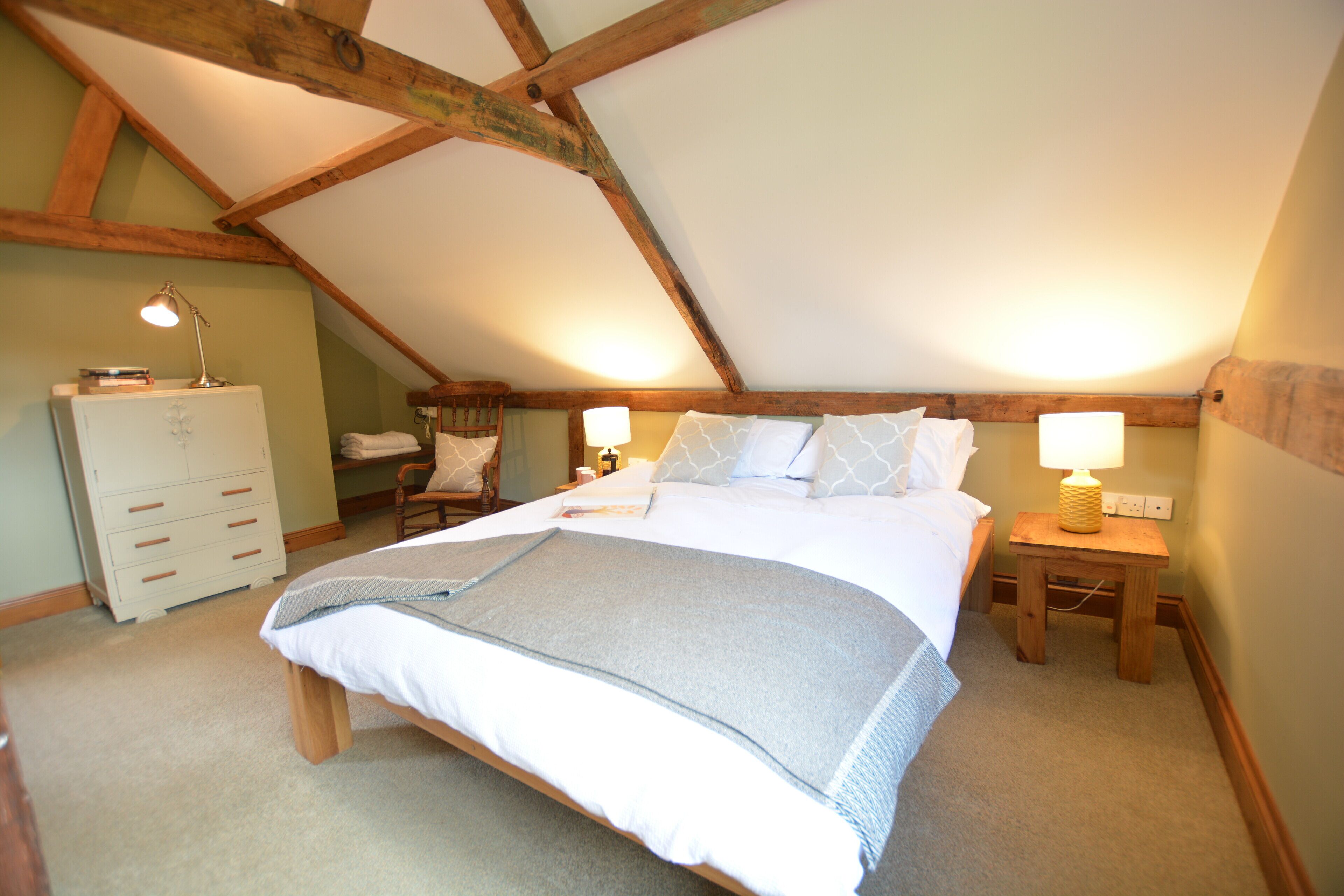 Une chambre à coucher avec un grand lit, deux tables de chevet avec des lampes, une commode en bois et une chaise.