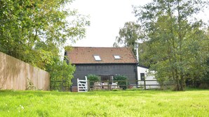 A house with a sloped roof, two small windows, and a wooden fence. - Wheelwright's Barn (Halesworth)