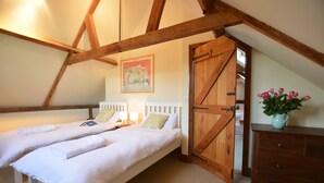 A bedroom with two beds, wooden beams, a wooden door, a dresser, and a vase with flowers. - Wheelwright's Barn (Halesworth)