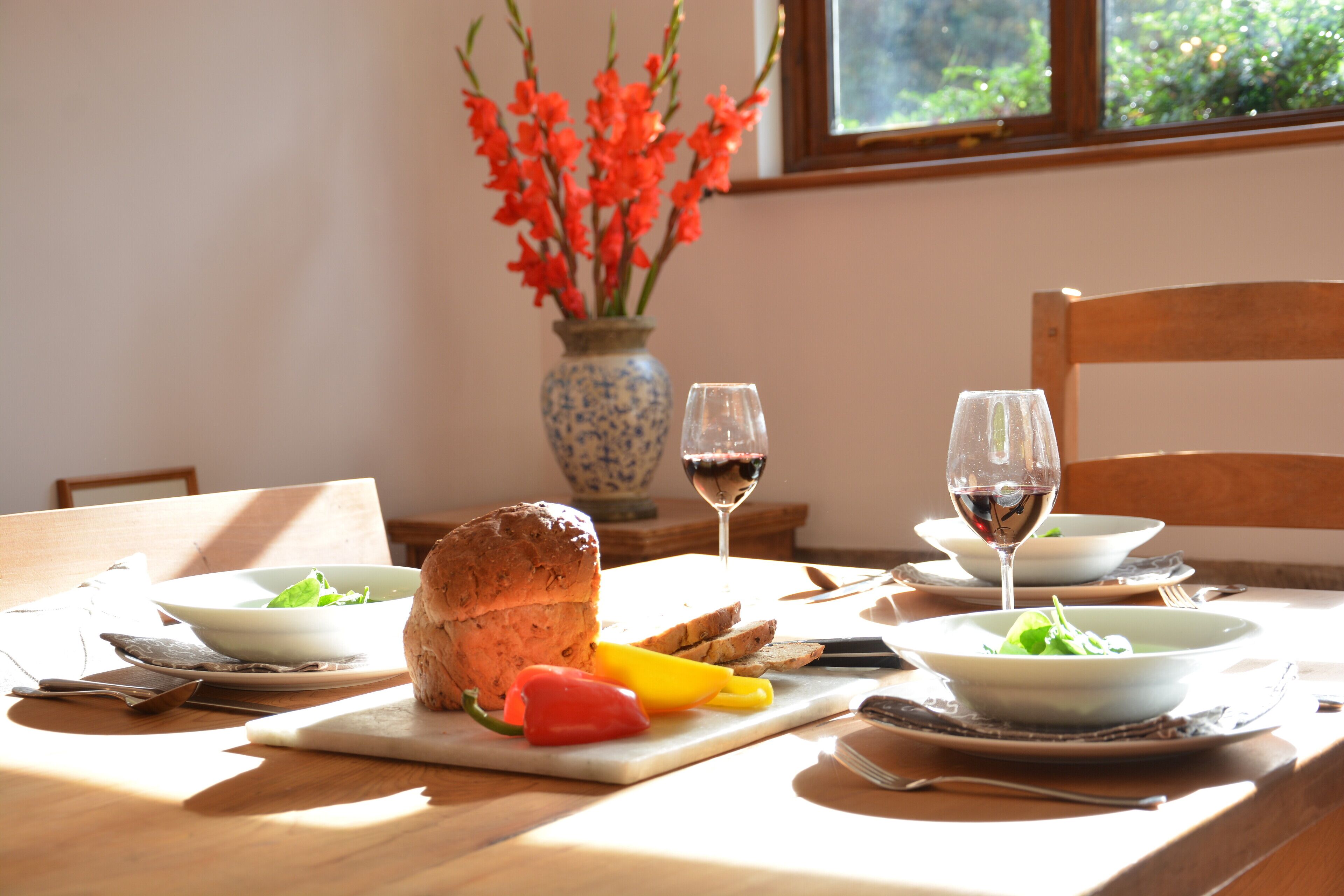 A dining table with bread, sliced bread, a red bell pepper, and a yellow bell pepper. There are two wine glasses with red wine.