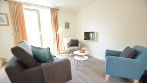 Ein modernes Wohnzimmer mit zwei Sofas, einem kleinen runden Tisch und einem an der Wand befestigten Fernseher.