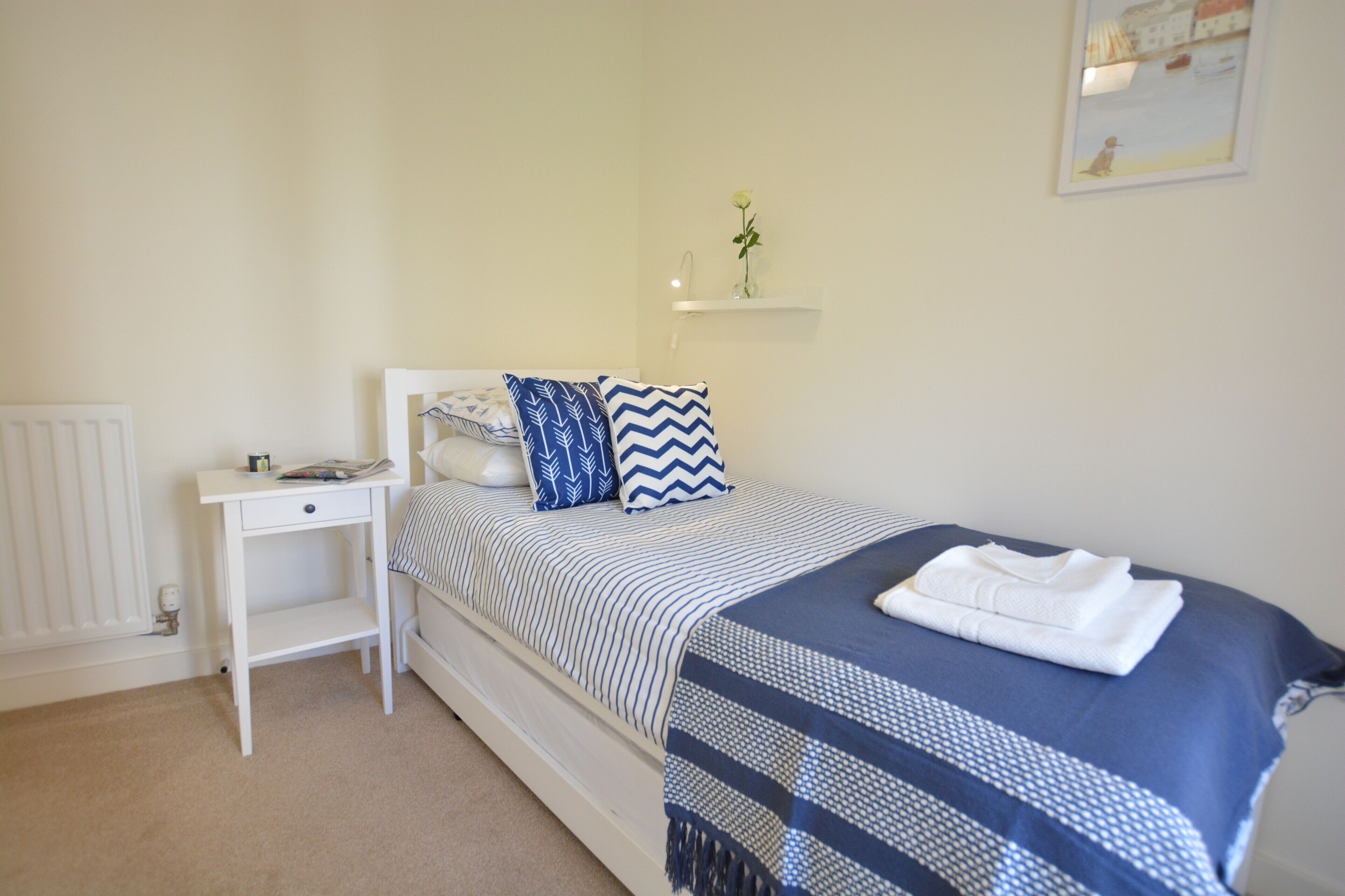 A bedroom with a bed, a bedside table, a radiator, and a wall-mounted shelf with a flower.
