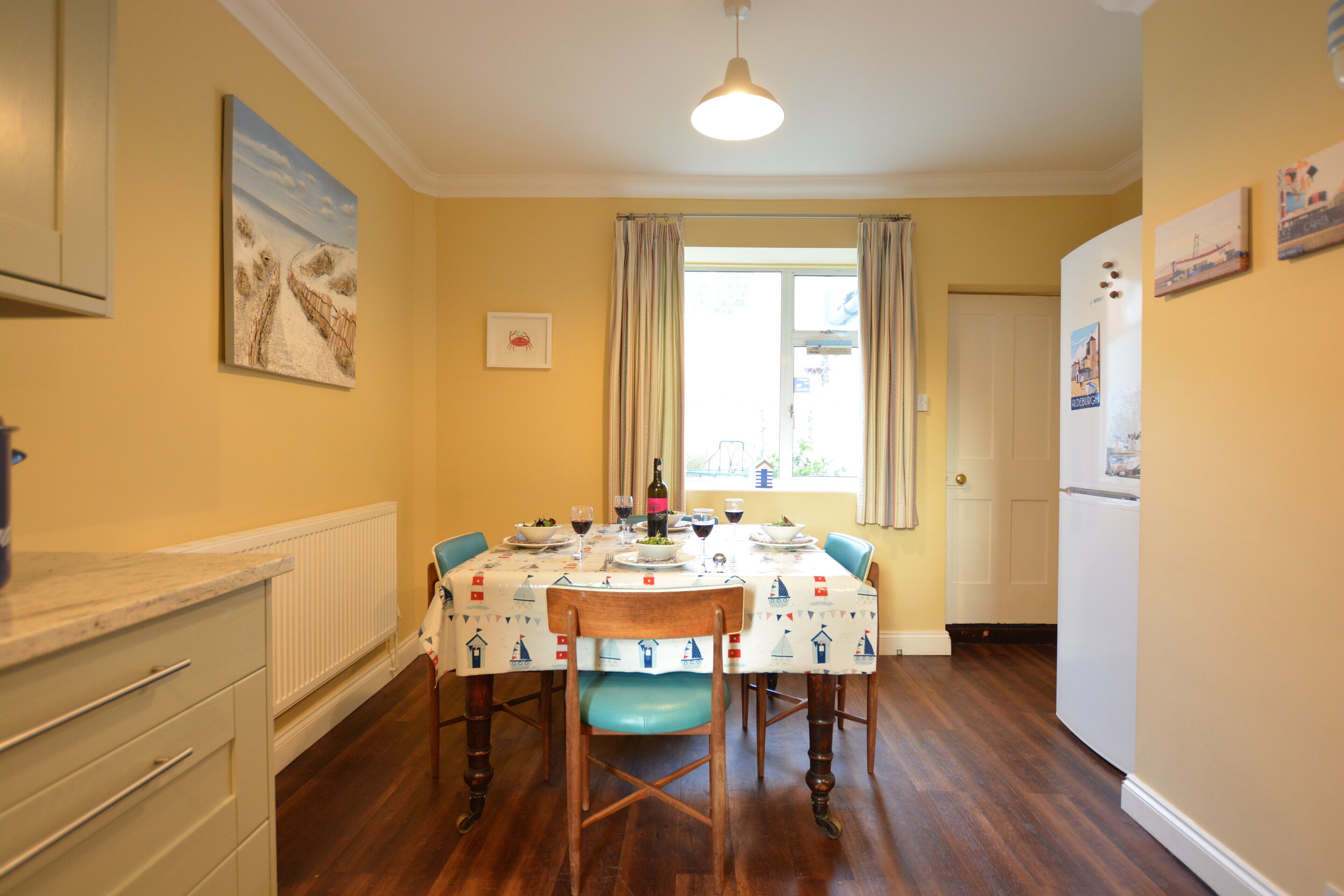 A dining area with a table set for four, wooden chairs, a white radiator, and a window with curtains.