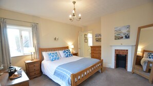 A bedroom with a wooden bed, bedside tables, a dresser, a fireplace, and a large mirror. - Gosfield Cottage, Aldeburgh (Aldeburgh)