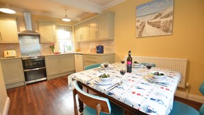 A kitchen with wooden cabinets, a dining table set for four, and a painting on the wall. - Gosfield Cottage, Aldeburgh (Aldeburgh)