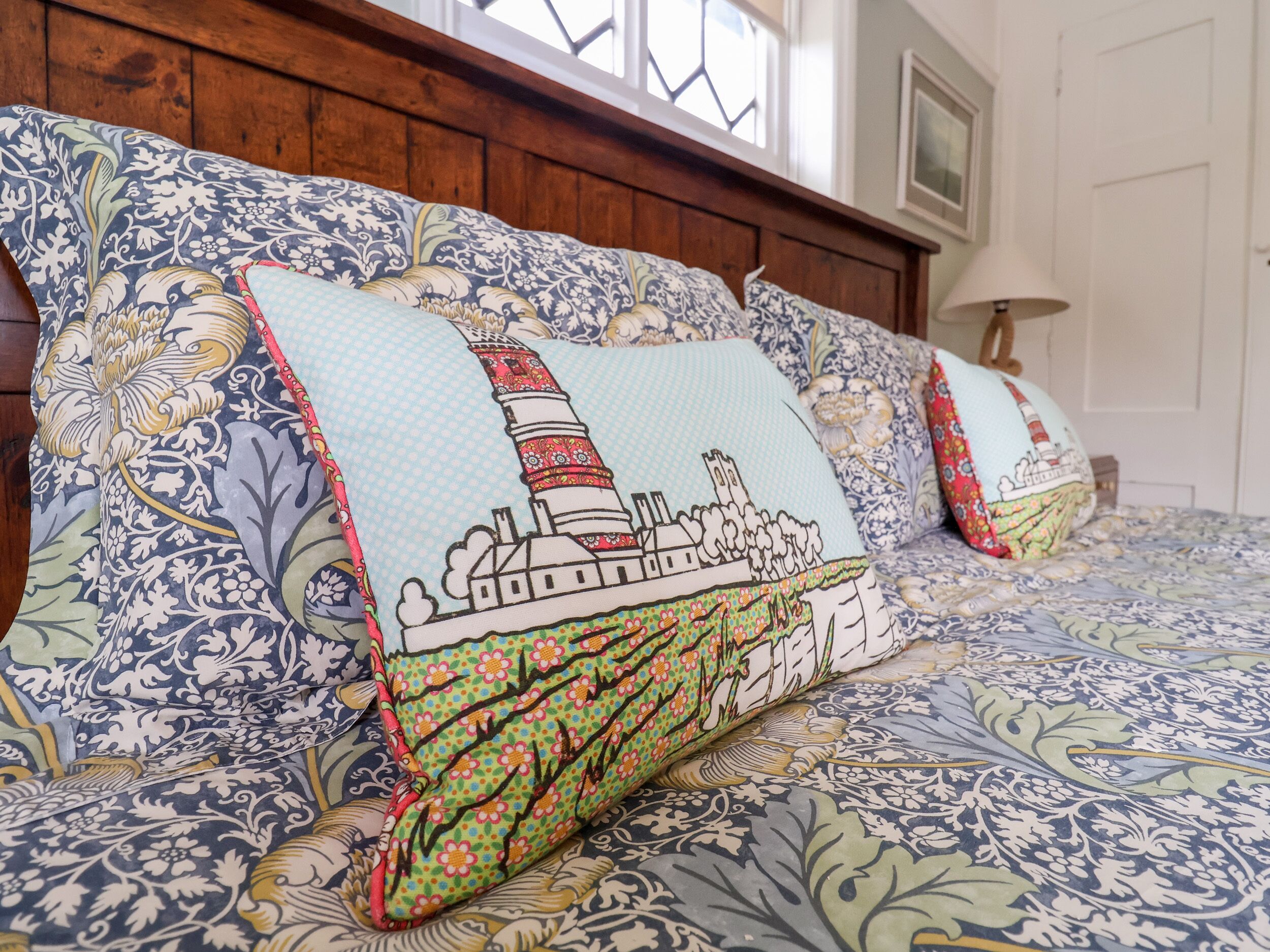 A bed with patterned bedding and pillows featuring a lighthouse design.