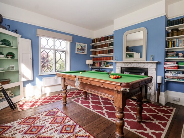 A room with a pool table, bookshelves, a fireplace, and a window with a view.