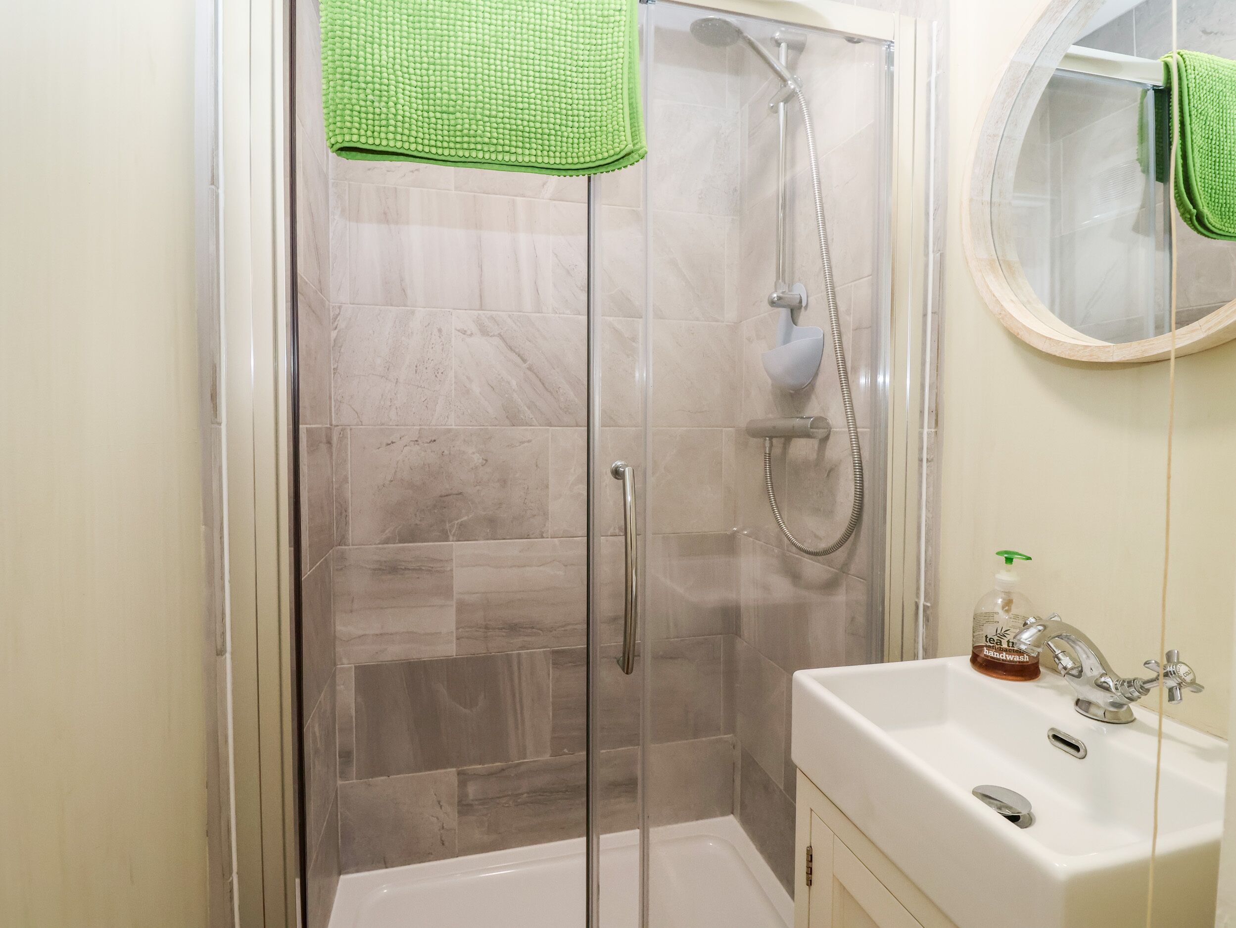 Un baño con ducha de vidrio, un lavabo blanco con dispensador de jabón y un espejo sobre el lavabo.