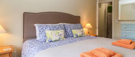 A neatly made bed with floral-patterned pillows, a bedside lamp, and a folded towel on the bed.