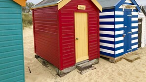 Drei Strandhütten in verschiedenen Farben und mit unterschiedlichen Namen: rot, mit dem Schriftzug 'Queenie', blau, mit dem Schriftzug 'Elizabeth', und türkis.