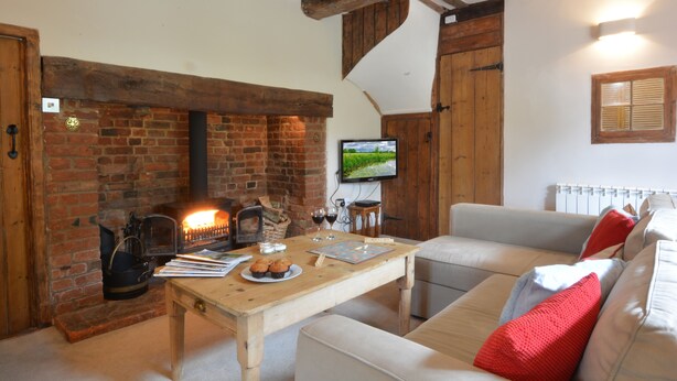 Ein gemütliches Wohnzimmer mit Kamin aus Ziegelsteinen, einem an der Wand befestigten Fernseher und einer bequemen Couch mit roten Kissen.