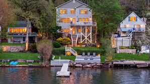 A lakeside house with a dock, a second-story balcony, and a stone retaining wall.