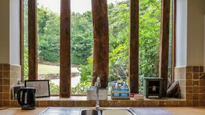 A kitchen with a sink, a coffee maker, and a window with a view of greenery. - Quill Farm Barn (Woodbridge)
