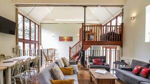 A spacious living area with a high ceiling, a dining table with chairs, a sofa set, and a staircase leading to an upper level. - Quill Farm Barn (Woodbridge)