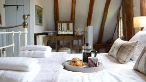 Quarto acolhedor com cama, almofadas, bandeja com doces, cafeteira e escrivaninha de madeira com cadeira.