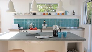 Una cocina moderna con una isla central, dos taburetes de bar y un ventanal con vistas a zonas verdes.