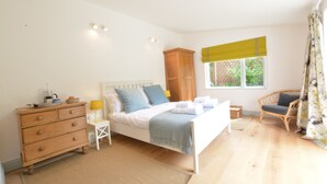 Un dormitorio con cama, cómoda, mesita de noche, silla, ventana y cortinas.