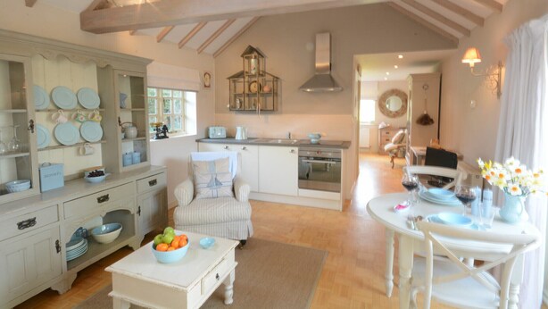 A spacious kitchen with a dining area, wooden beams on the ceiling, and a view of the living room. - The Nookery at Snape Hall (Saxmundham)