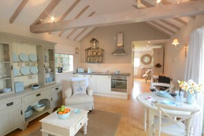 A spacious kitchen with a dining area, wooden beams on the ceiling, and a view of the living room. - The Nookery at Snape Hall (Saxmundham)