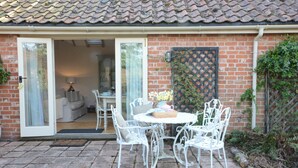 A patio with a white metal table and chairs, a brick wall, and a door leading to an interior space. - The Nookery at Snape Hall (Saxmundham)
