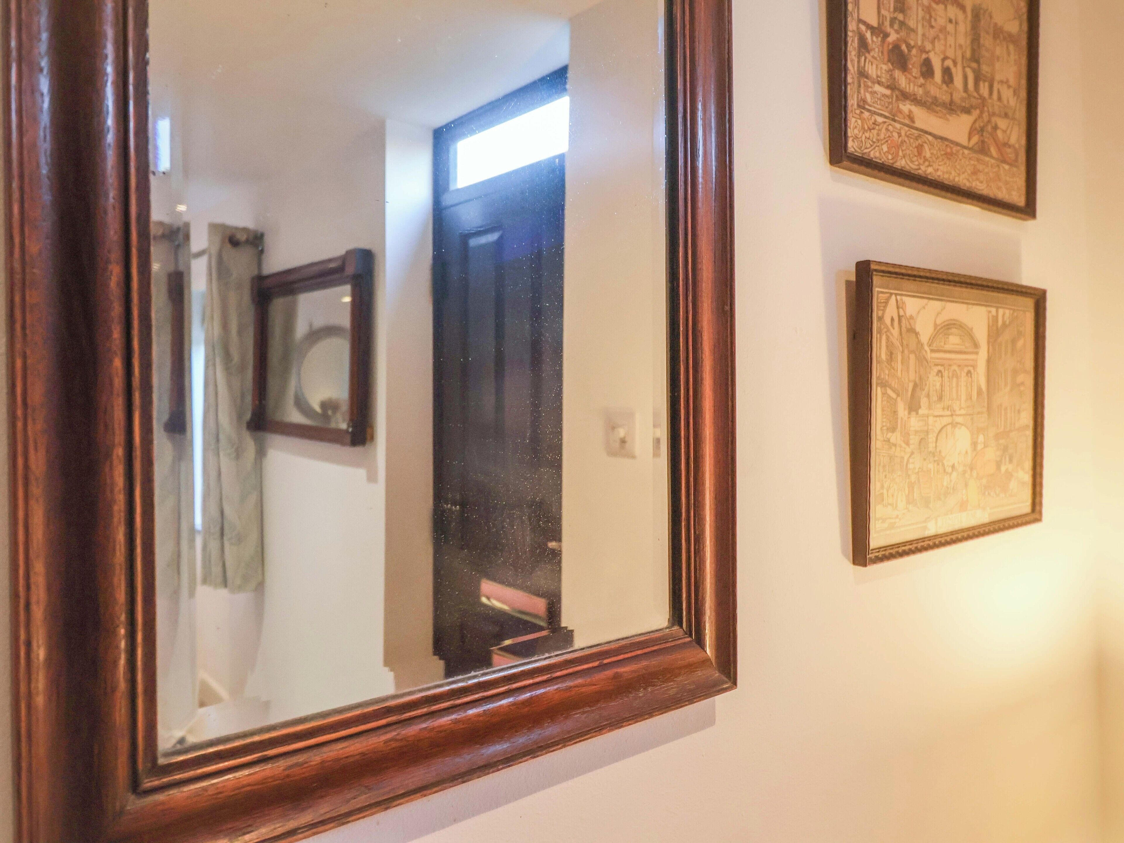 A mirror with a wooden frame, a door, and two framed pictures on the wall.